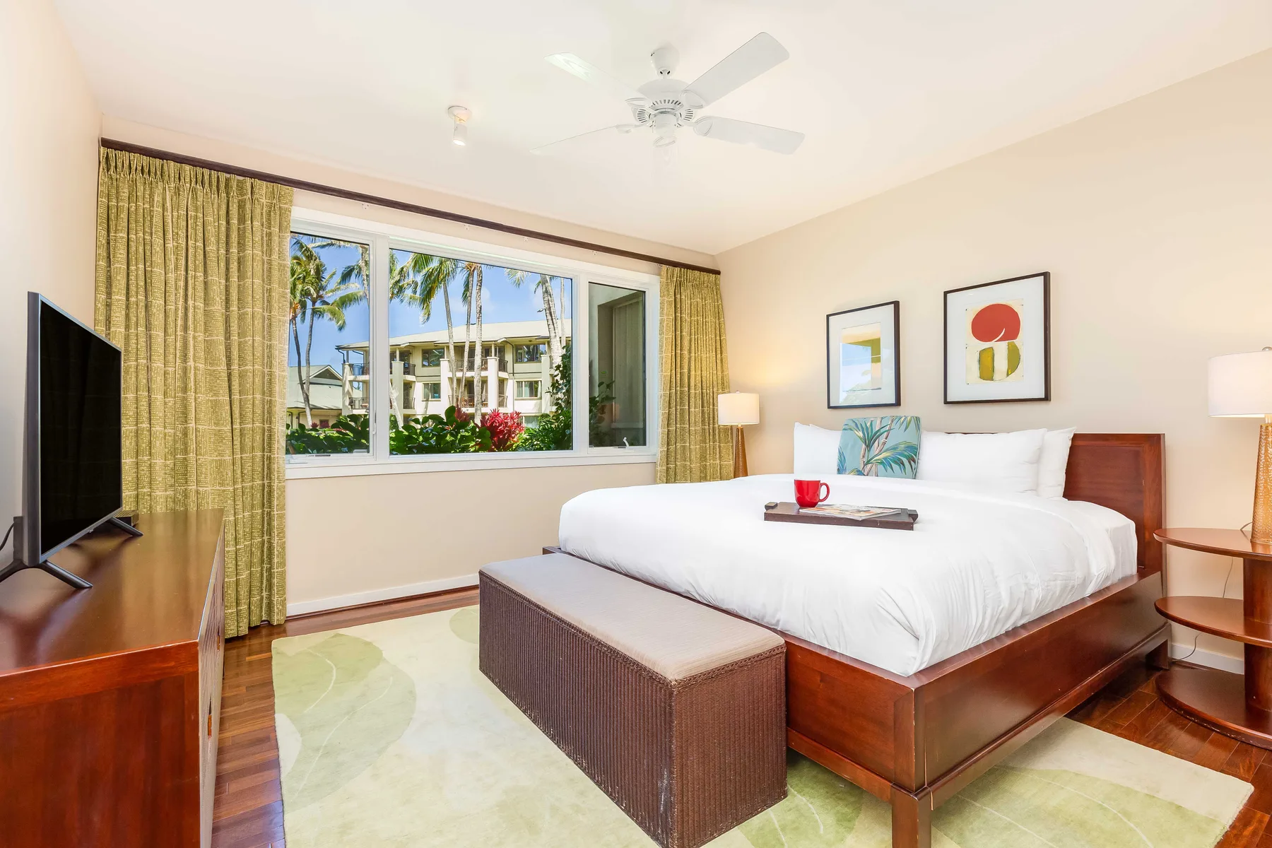 Un dormitorio luminoso con una cama bien hecha y una ventana amplia con palmeras a la vista.