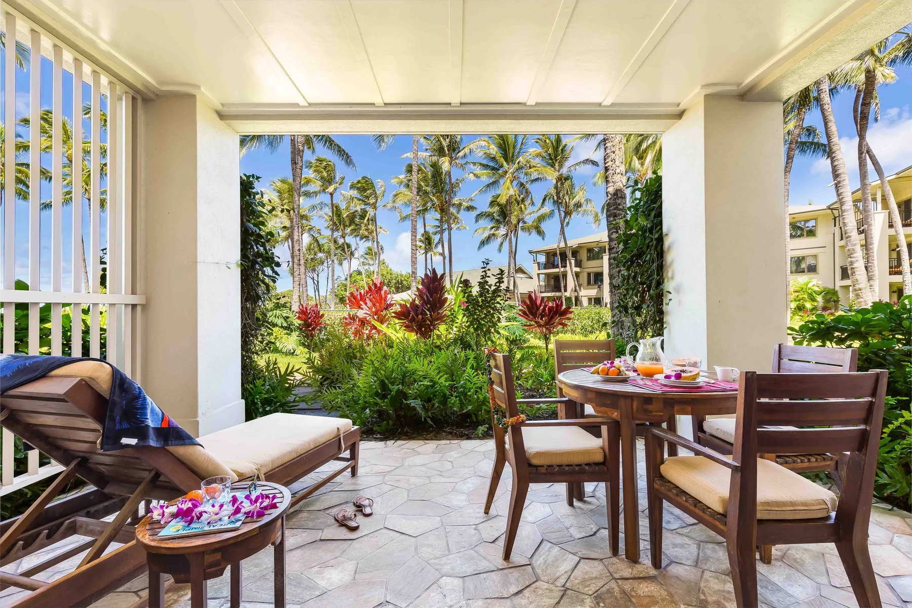 Un patio cubierto con asientos de comedor da a jardines tropicales y palmeras.