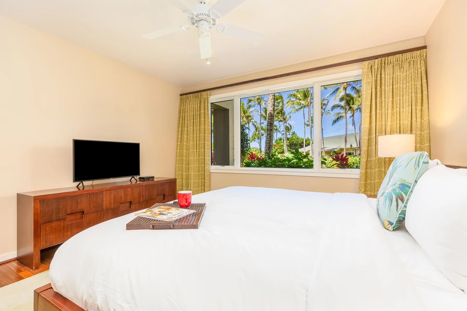 Un dormitorio con una cama grande, un televisor y una ventana con vista a palmeras.