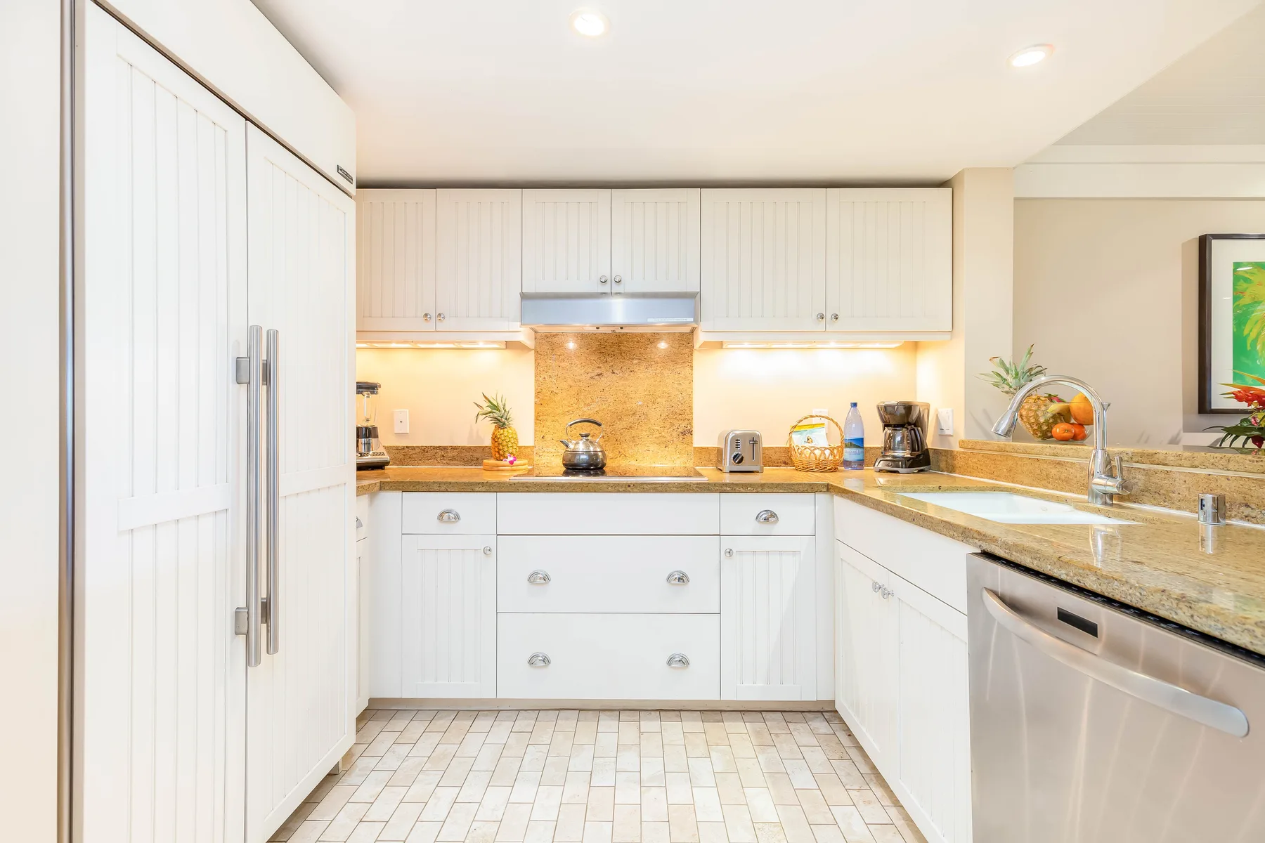 Una cocina luminosa con gabinetes blancos, encimeras claras y electrodomésticos de acero inoxidable.