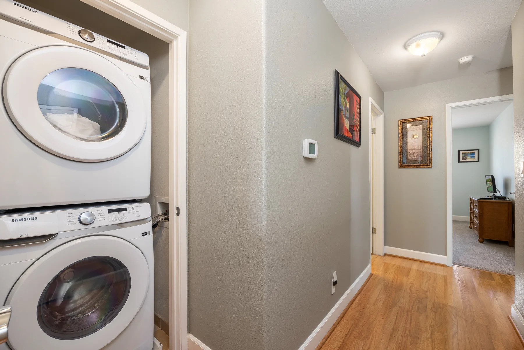 A narrow hallway with stacked laundry machines and framed artwork.