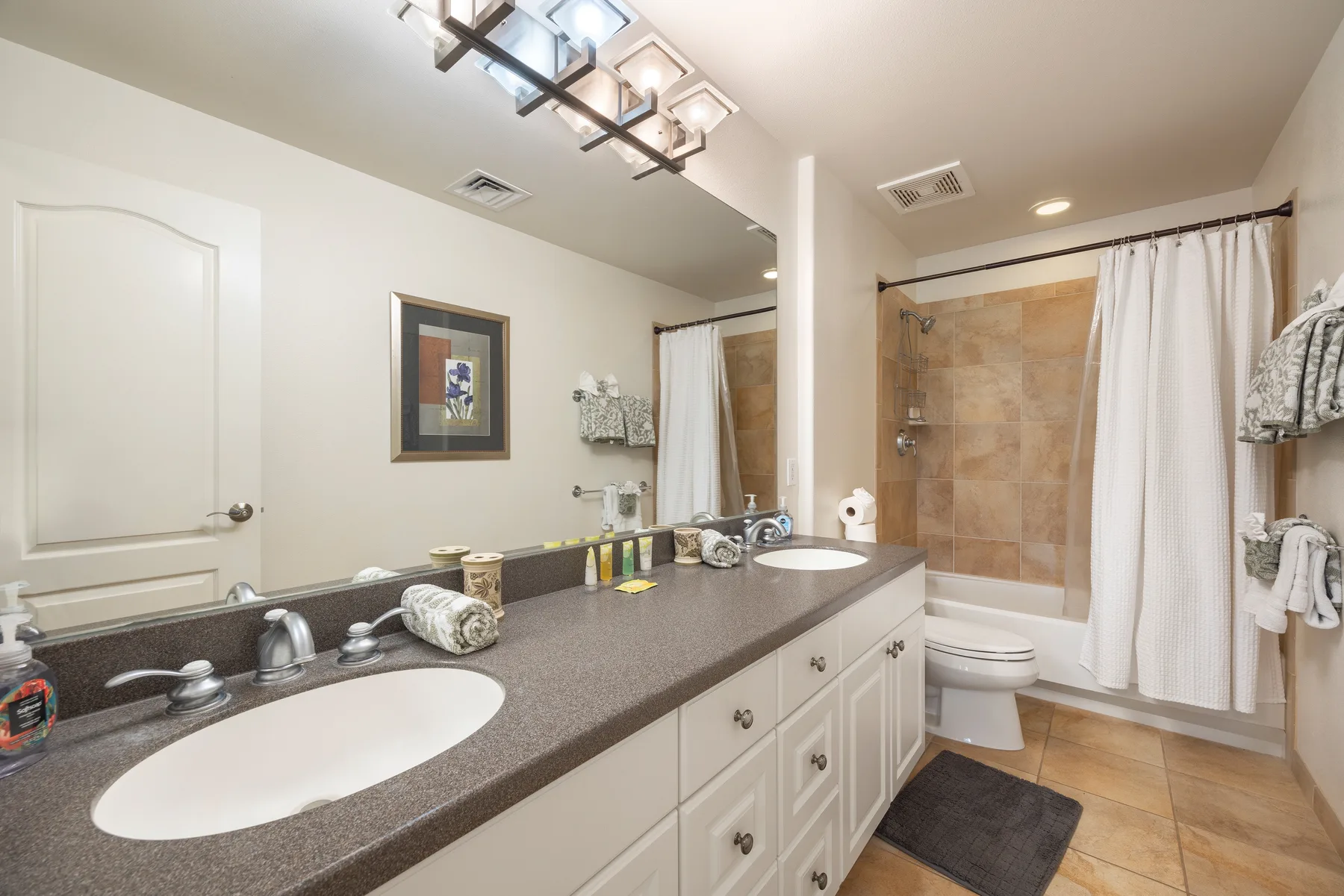 A bathroom with a long vanity, sink, and tiled shower area.