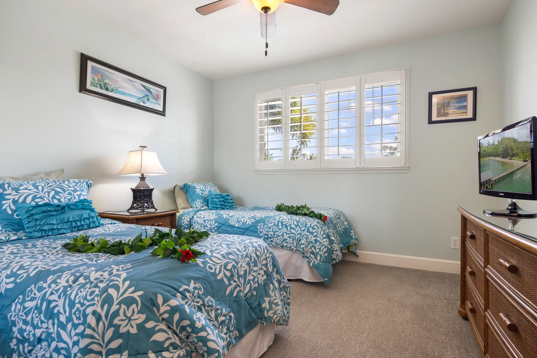 A bedroom with two beds dressed in blue patterned bedding and a window with shutters.