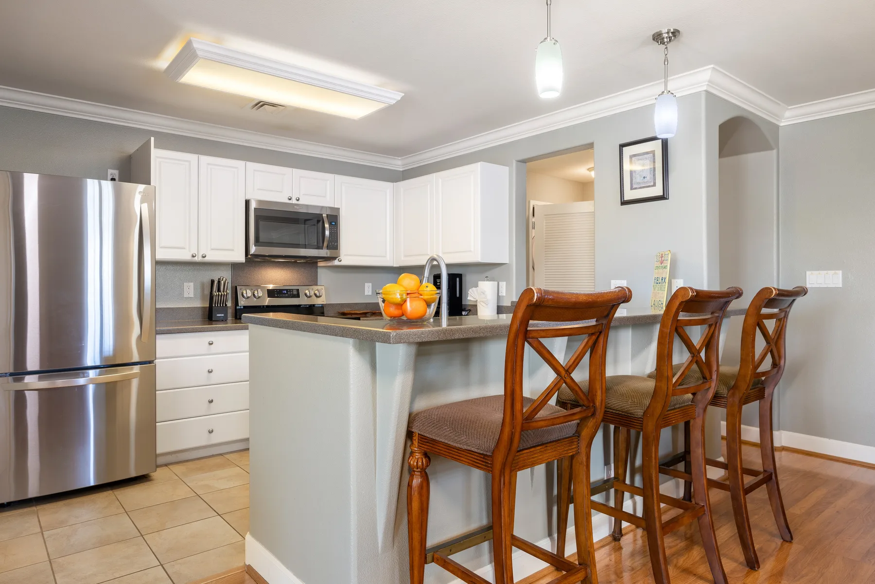 Una cocina luminosa con gabinetes blancos y una barra con asientos de madera.