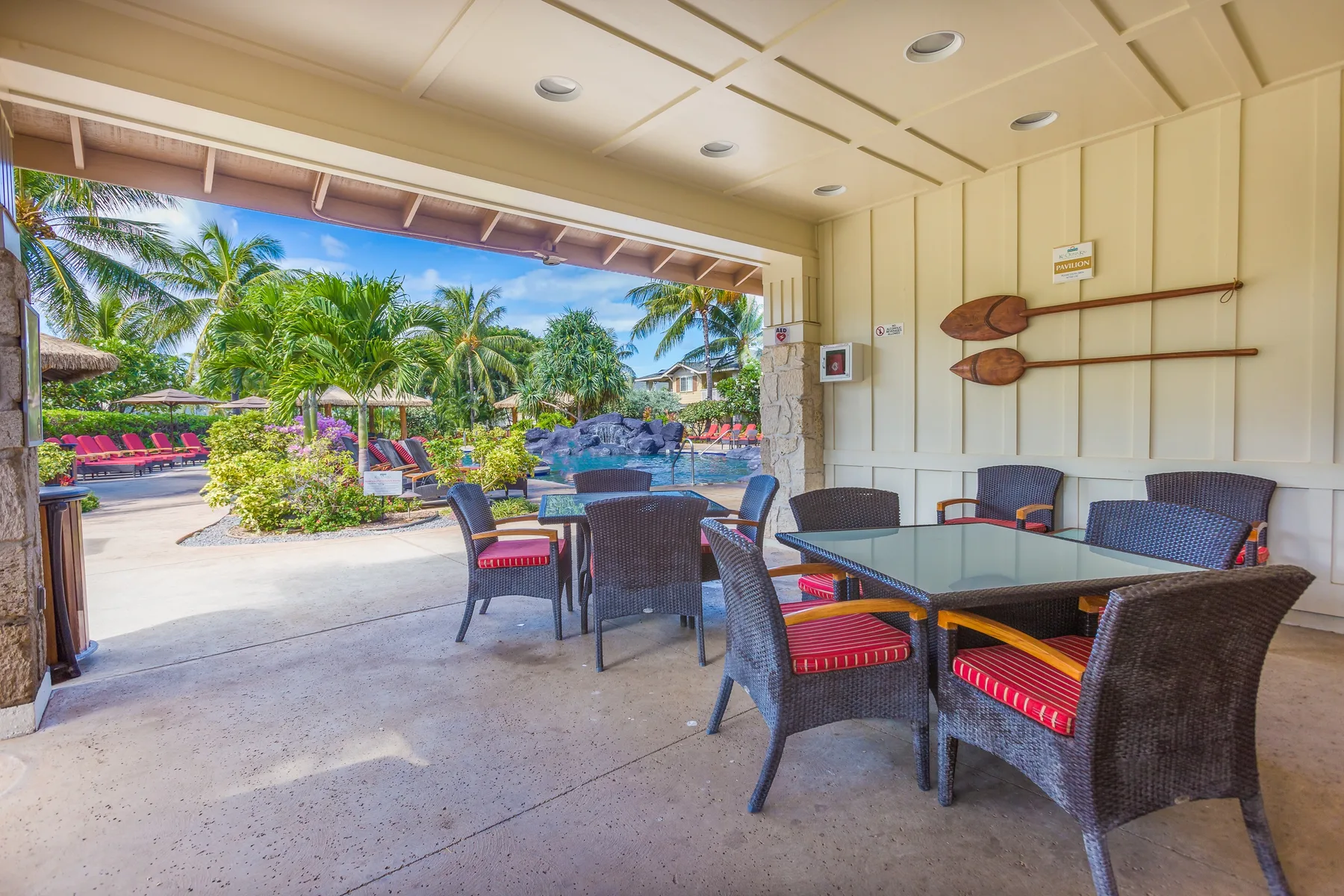A covered patio with outdoor seating opens onto a garden with palm trees.