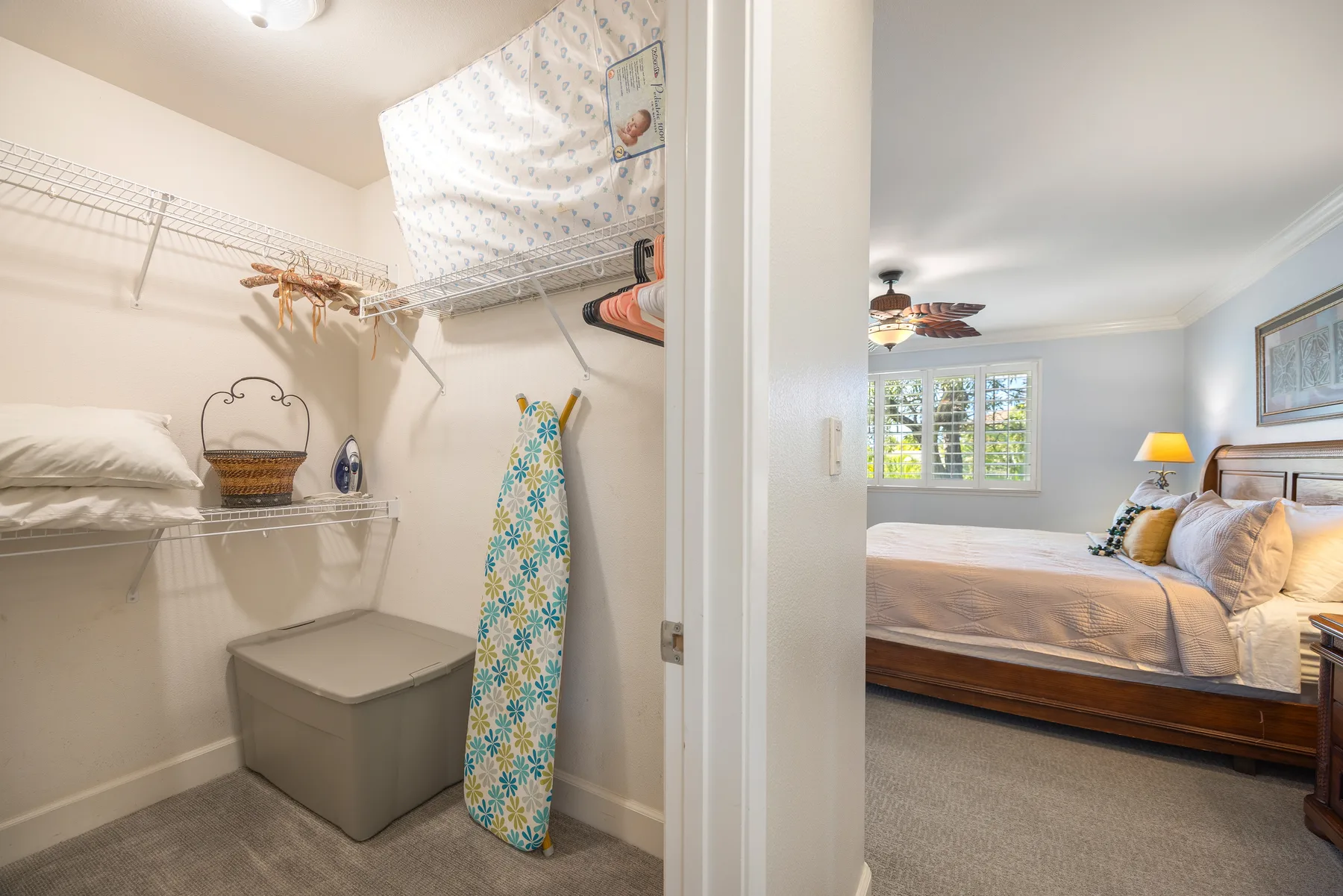 A bedroom with a bed beside an open closet containing shelves and hanging clothes.
