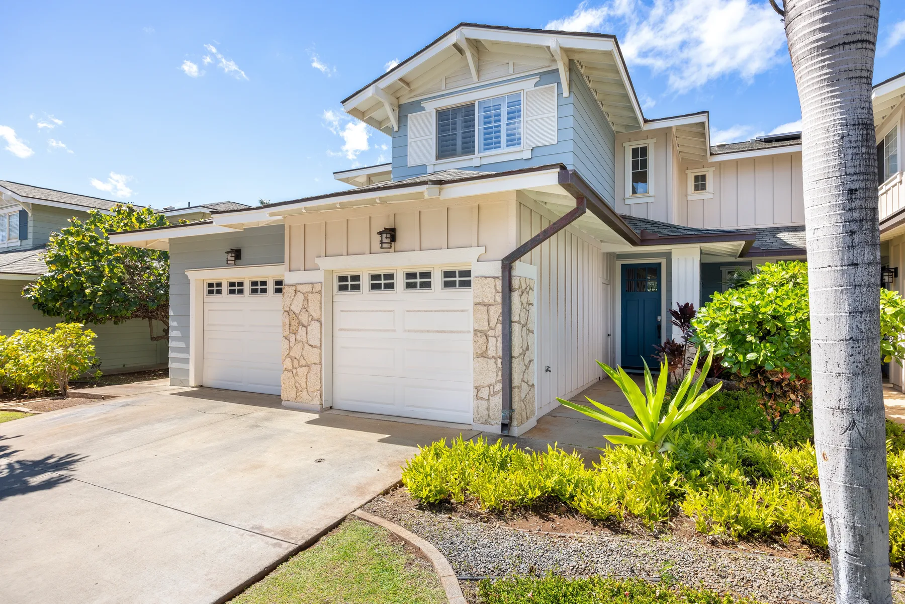 A light-colored house with a driveway, garage doors, and landscaped shrubs.