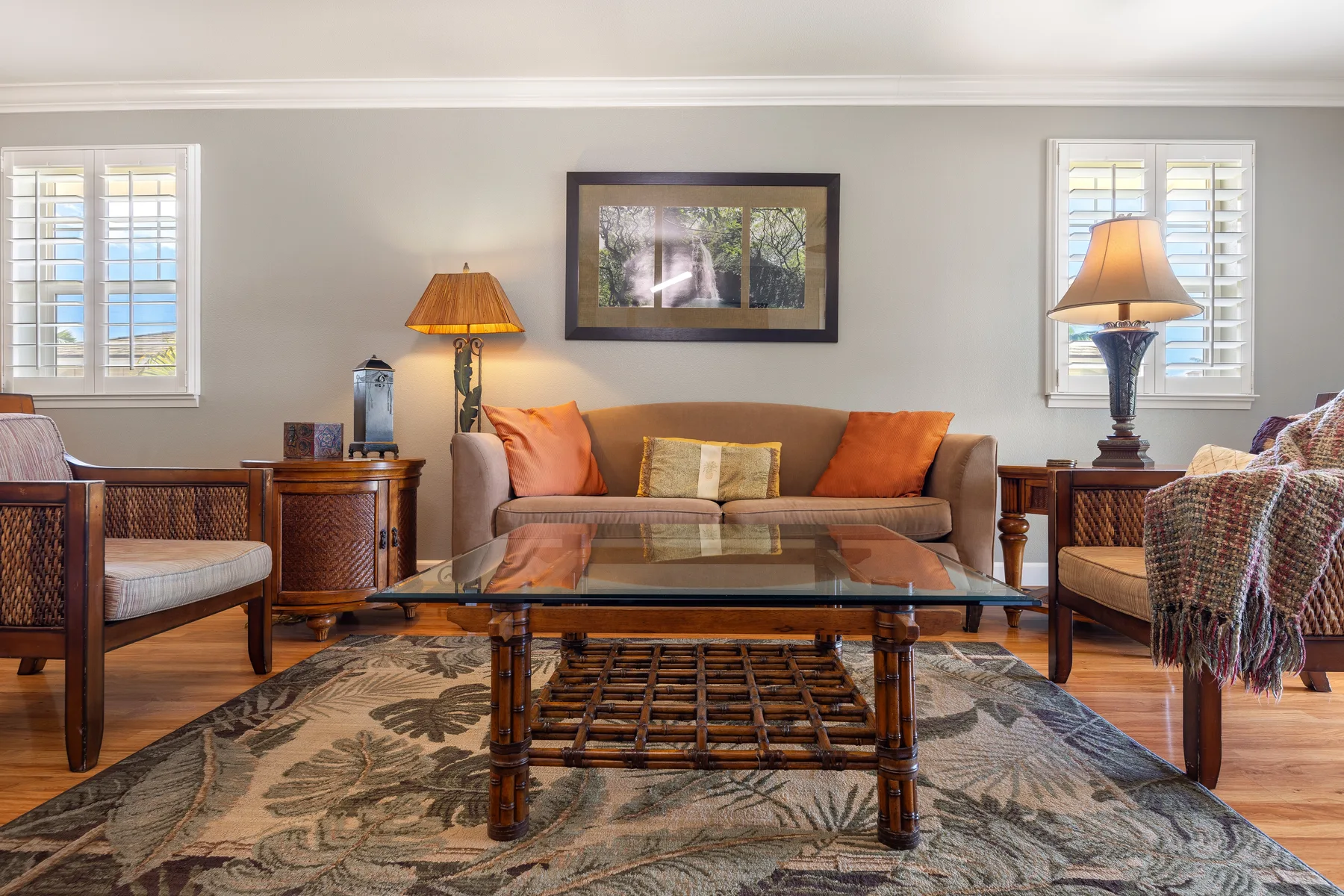 A living room with seating, a glass coffee table, and windows.