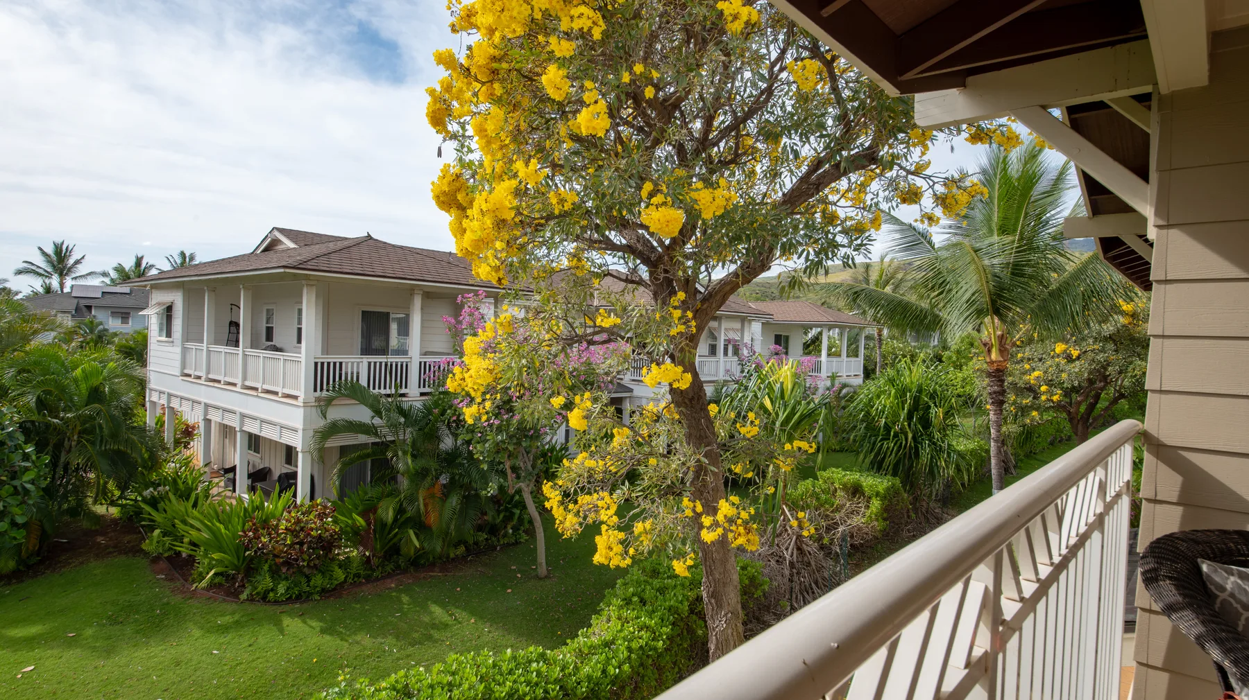 A covered balcony overlooks a garden with flowering trees and neighboring buildings.