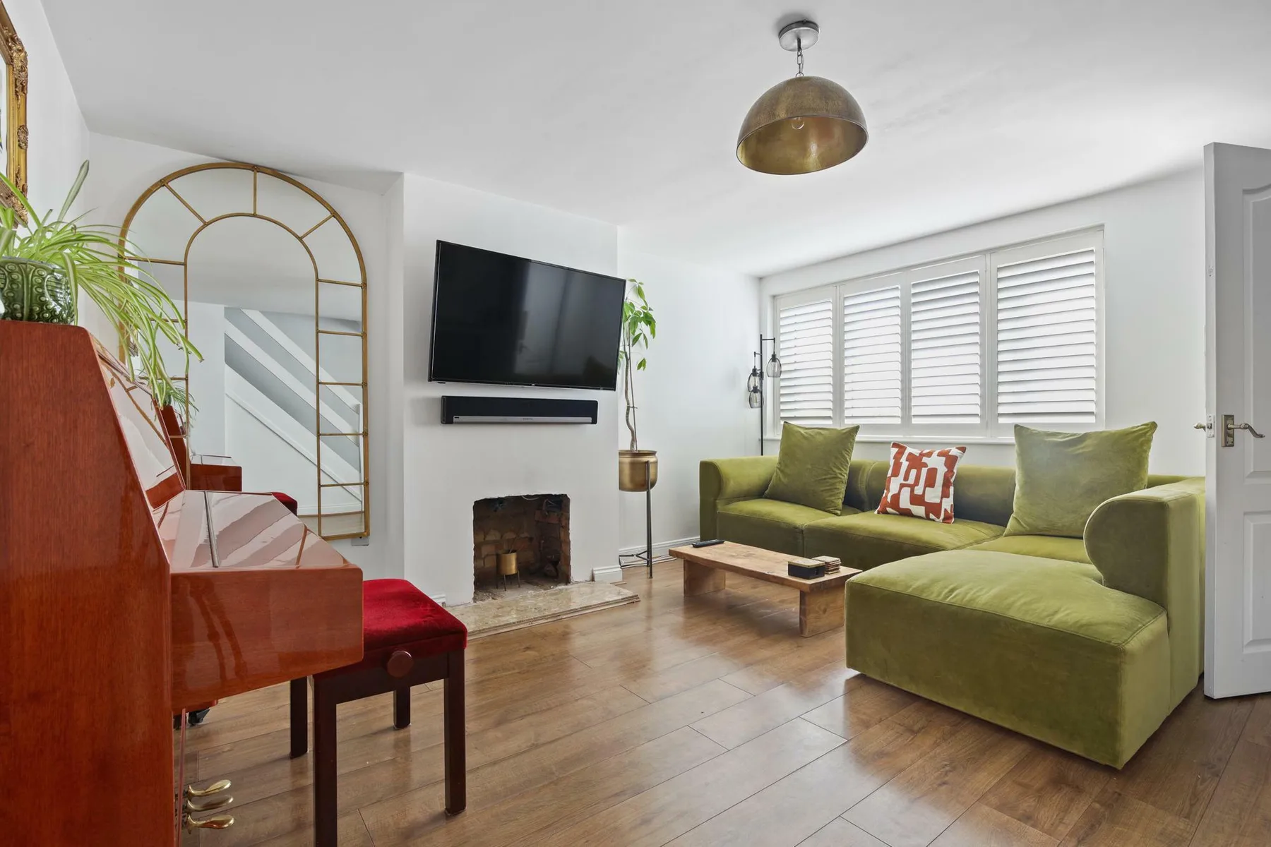 Una sala luminosa con asientos verdes, un televisor y un piano.