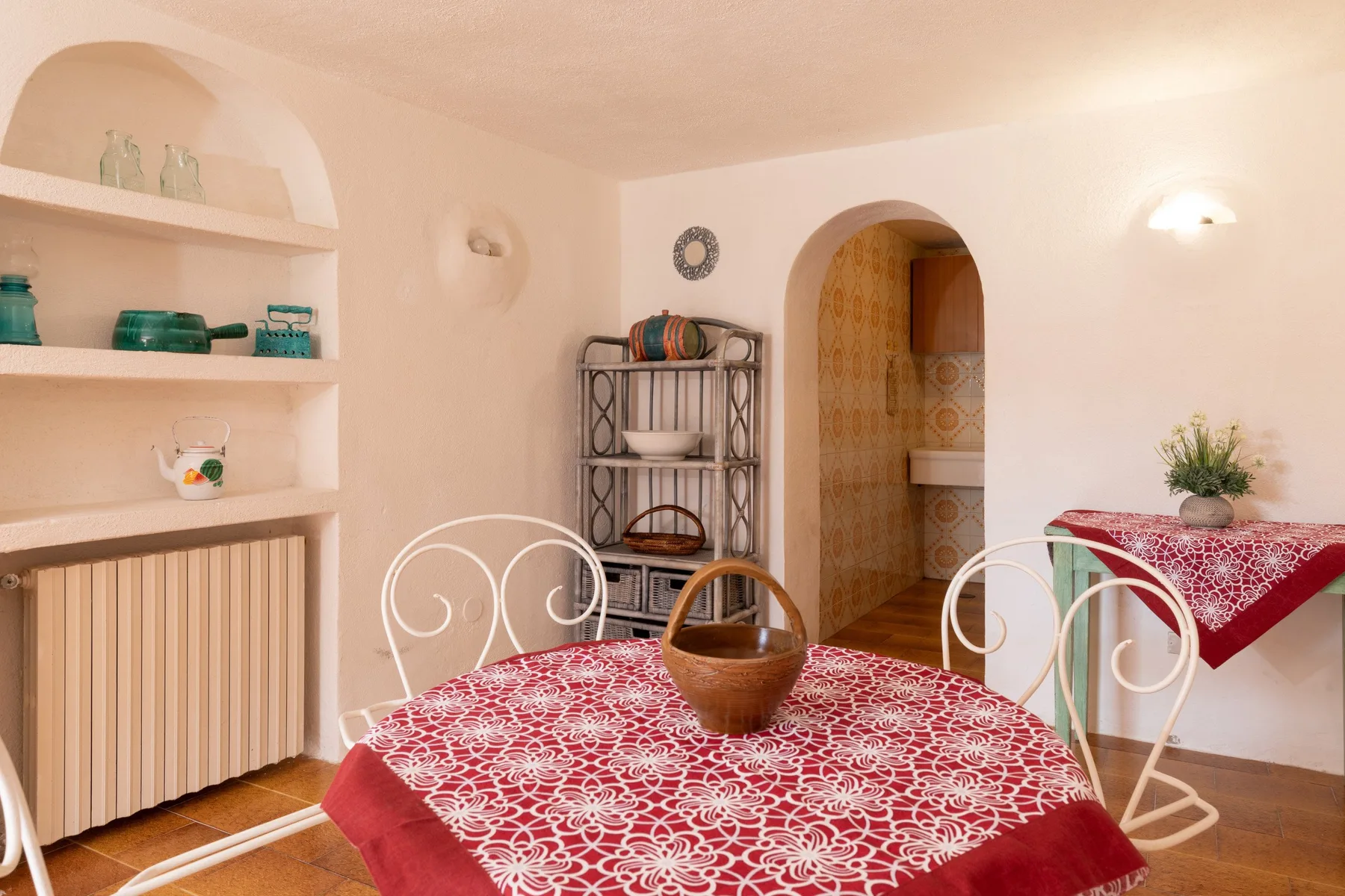 A dining area with a red patterned tablecloth and open wall shelves.
