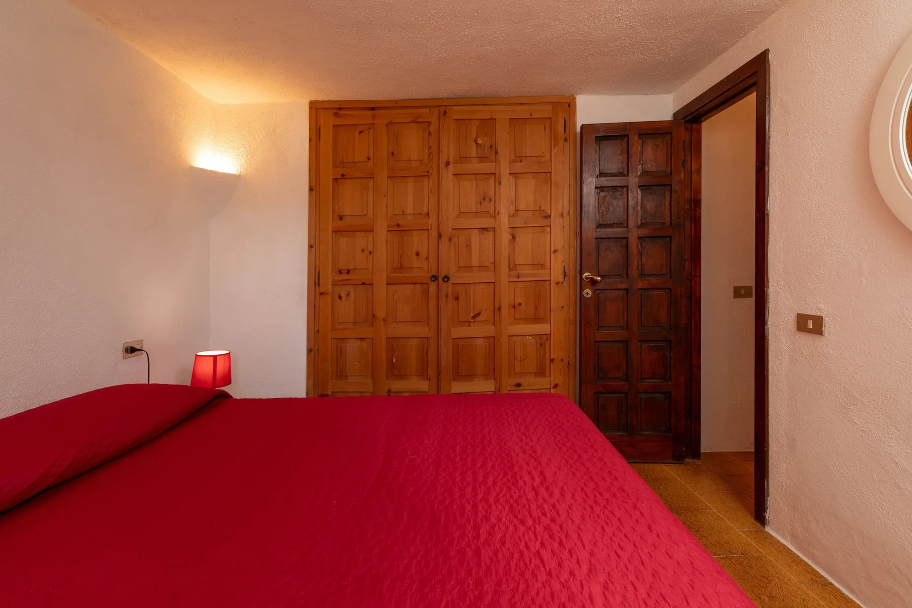 A bedroom with a red bedspread and wooden wardrobe.