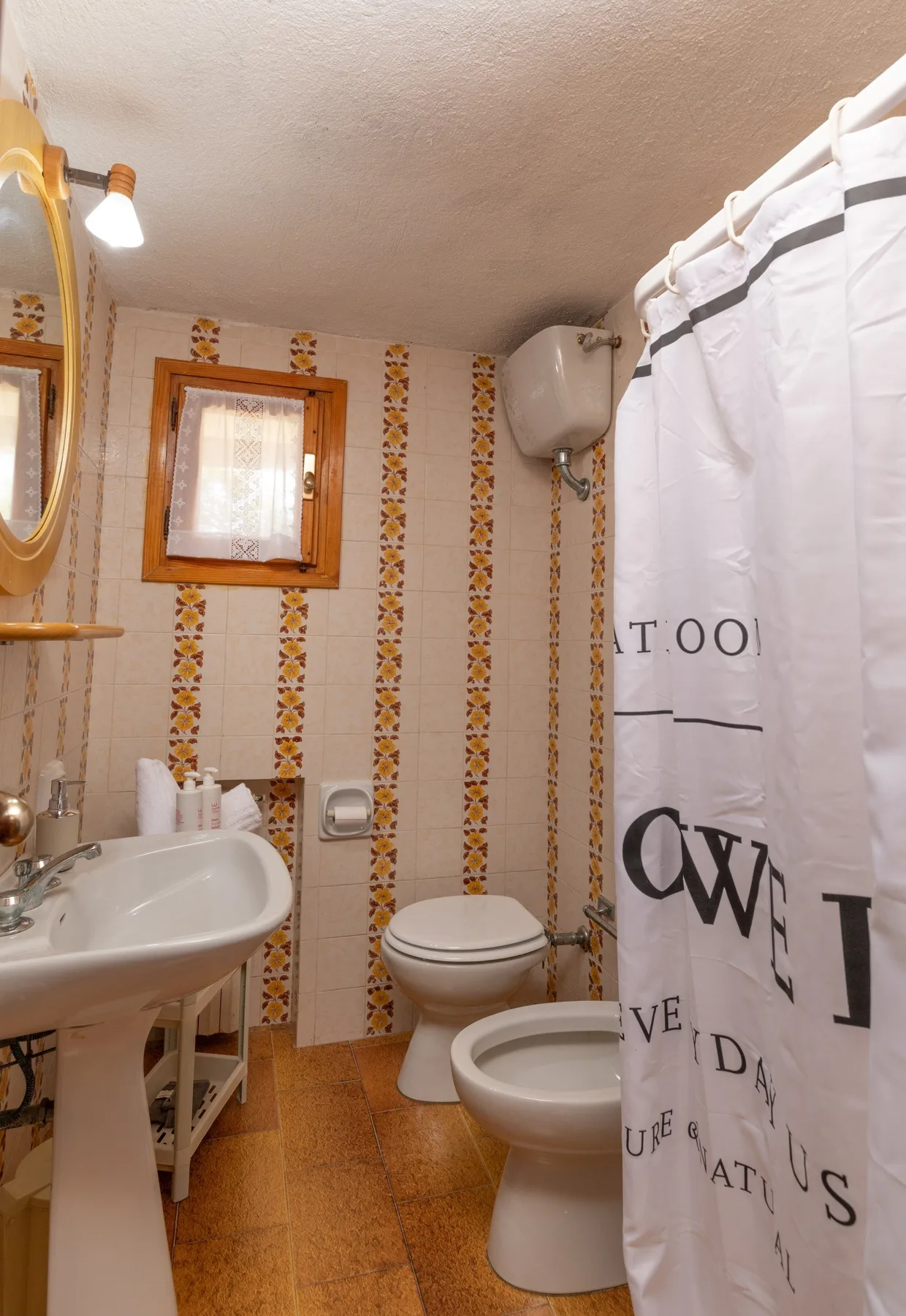 A bathroom with a sink, toilet, bidet, and patterned tile walls.