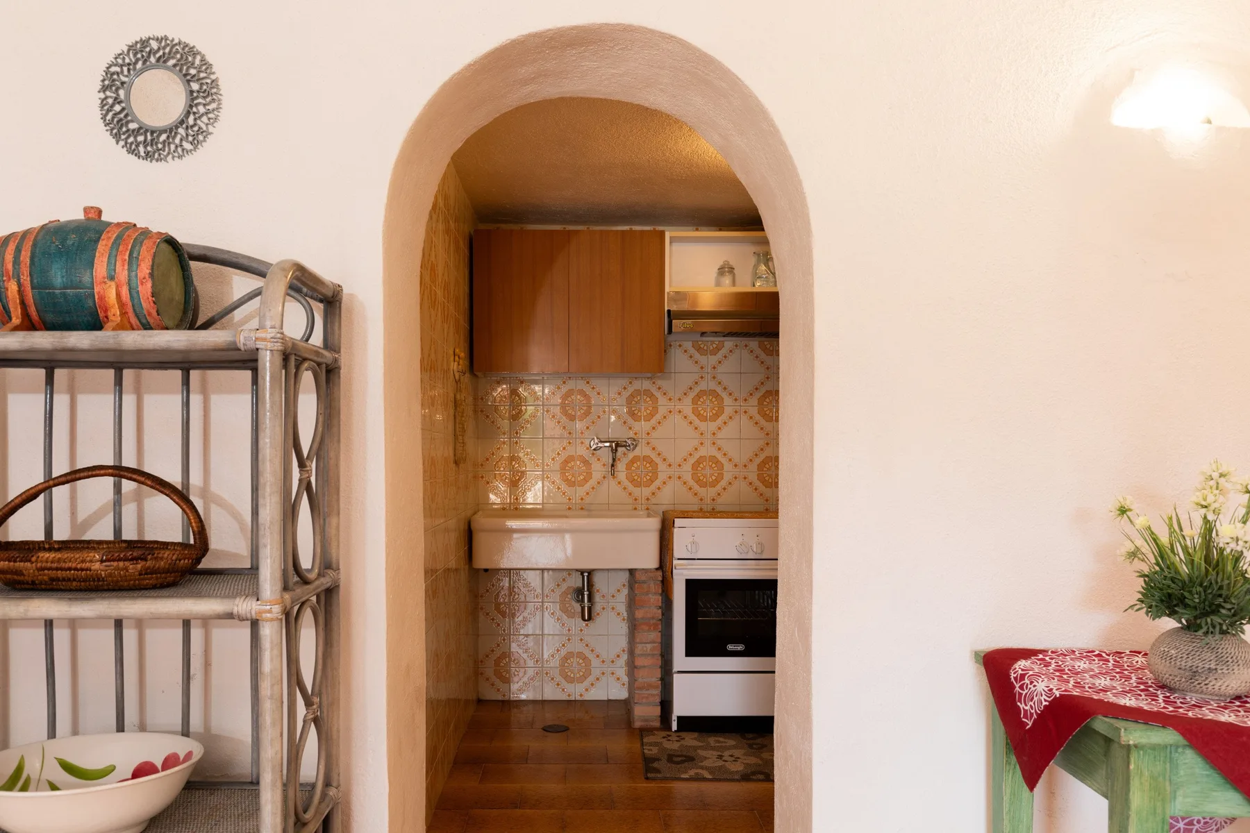 An arched kitchen doorway reveals patterned tile, wooden cabinets, and a countertop.