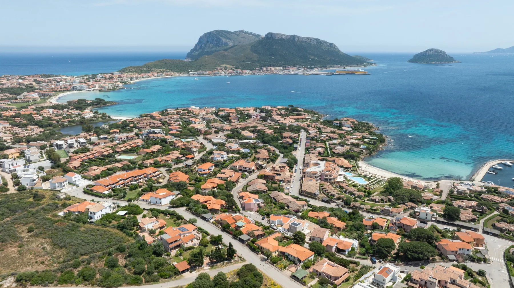 Aerial view of a coastal town with red-roofed buildings beside a blue bay.