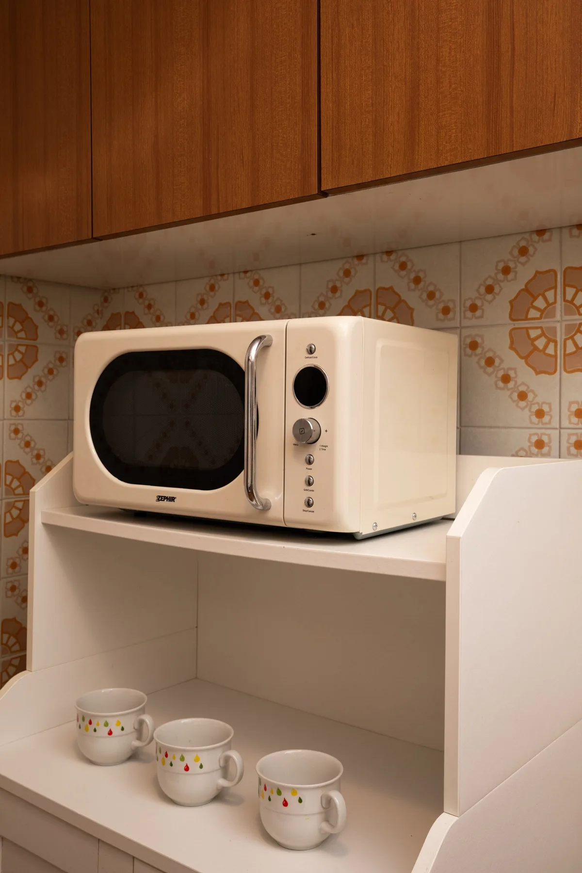 A kitchen counter holds a microwave and three cups beneath wooden cabinets.