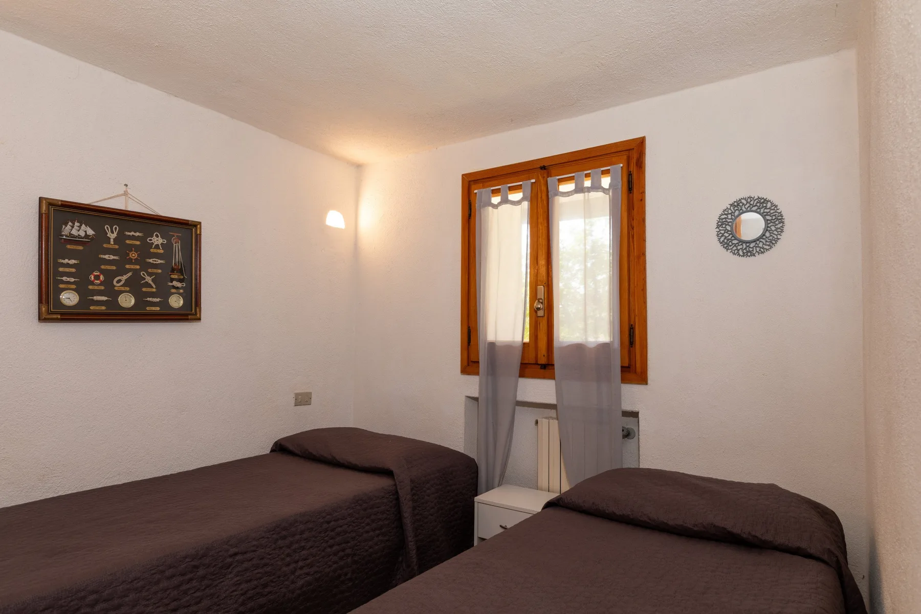 A bedroom with two beds, a curtained window, and framed wall art.