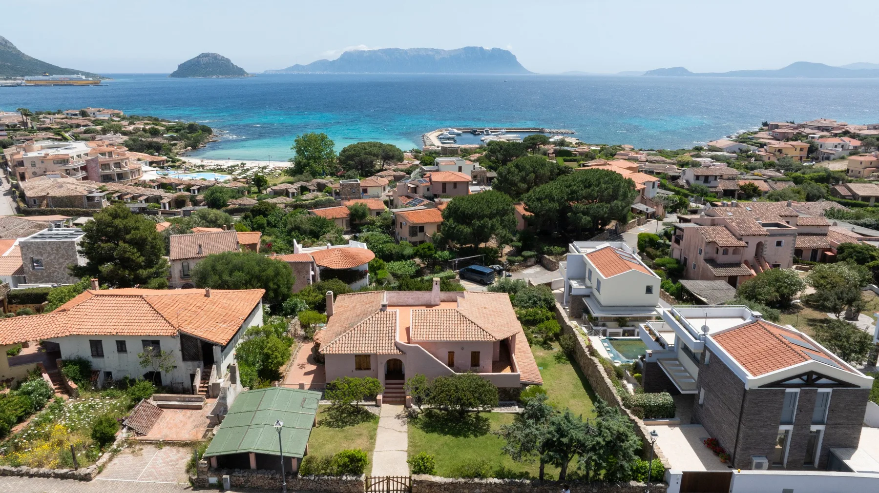 A coastal residential area with homes, greenery, and the sea beyond.