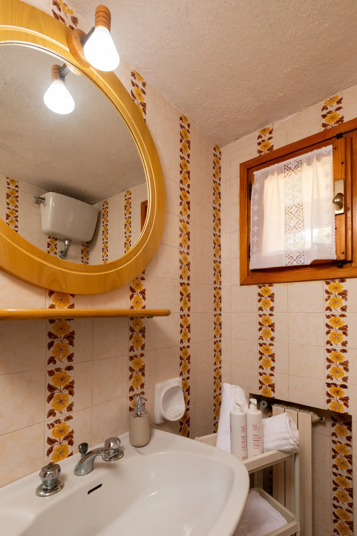 A bathroom with a white sink, large mirror, and small curtained window.