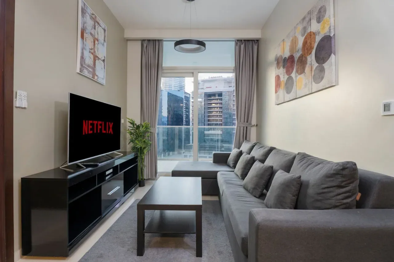 Una sala de estar con asientos, una mesa de centro y un televisor frente a una ventana grande.