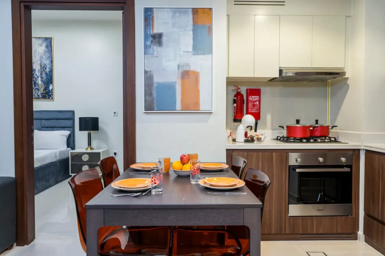 Una mesa de comedor está junto a una cocina compacta, con un dormitorio visible a través de la puerta.
