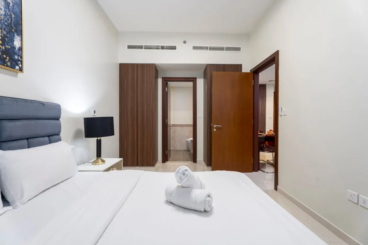 Un dormitorio con una cama bien tendida y puertas de madera abiertas.