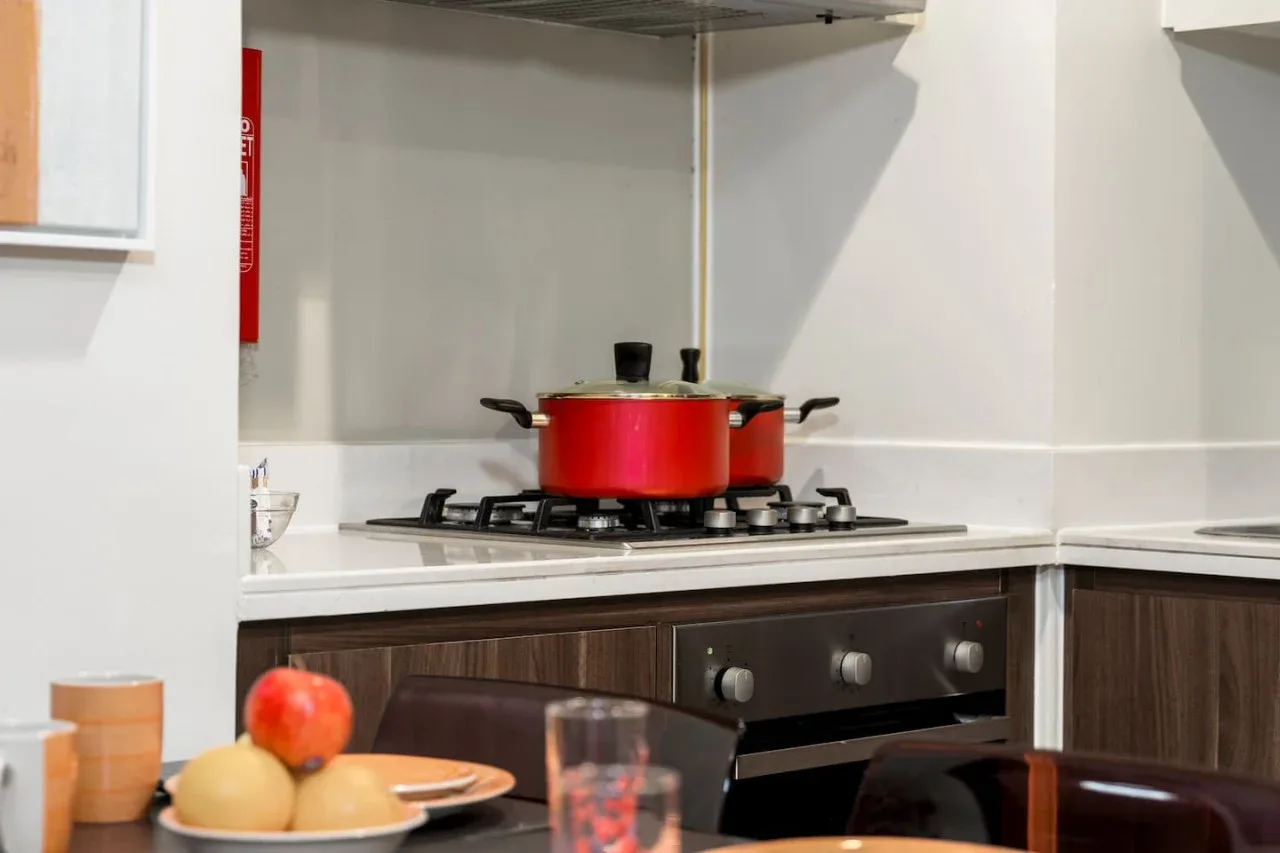 Una cocina con una olla roja sobre la estufa y asientos en primer plano.