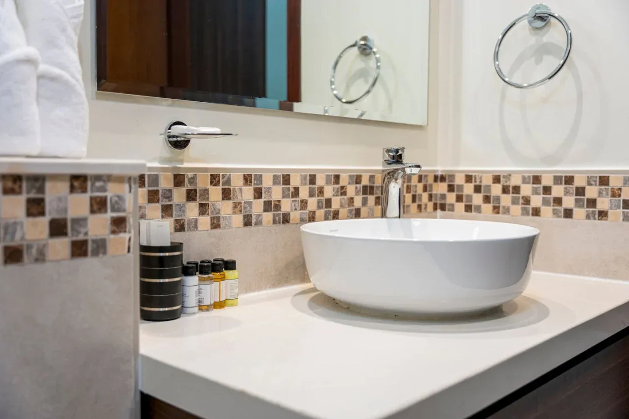 Un lavabo de baño con un lavabo blanco sobre encimera y un salpicadero de azulejos.