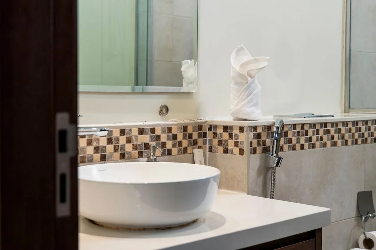 Un lavabo de baño con una pila blanca sobre encimera y pared de azulejos.