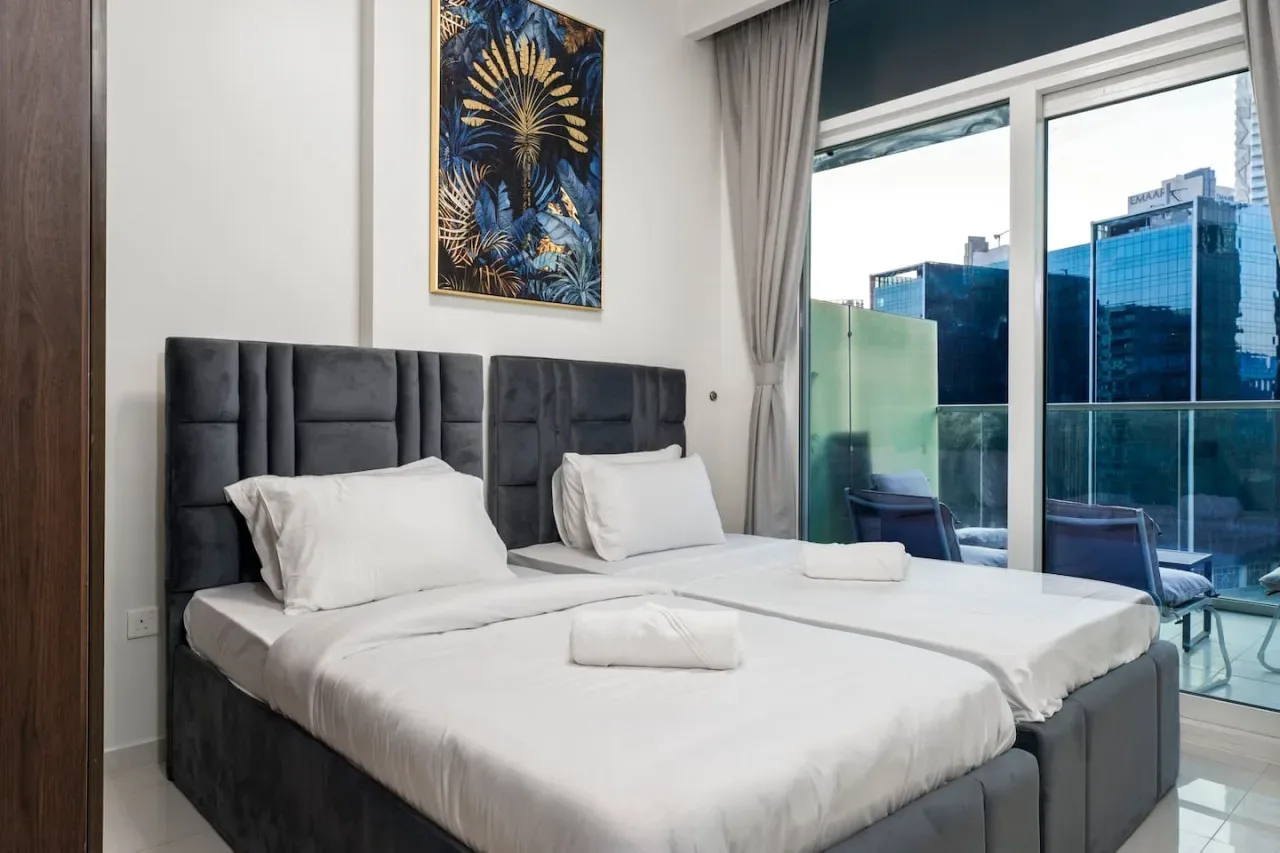 Un dormitorio con dos camas, ropa de cama blanca y puertas de cristal que dan a un balcón.