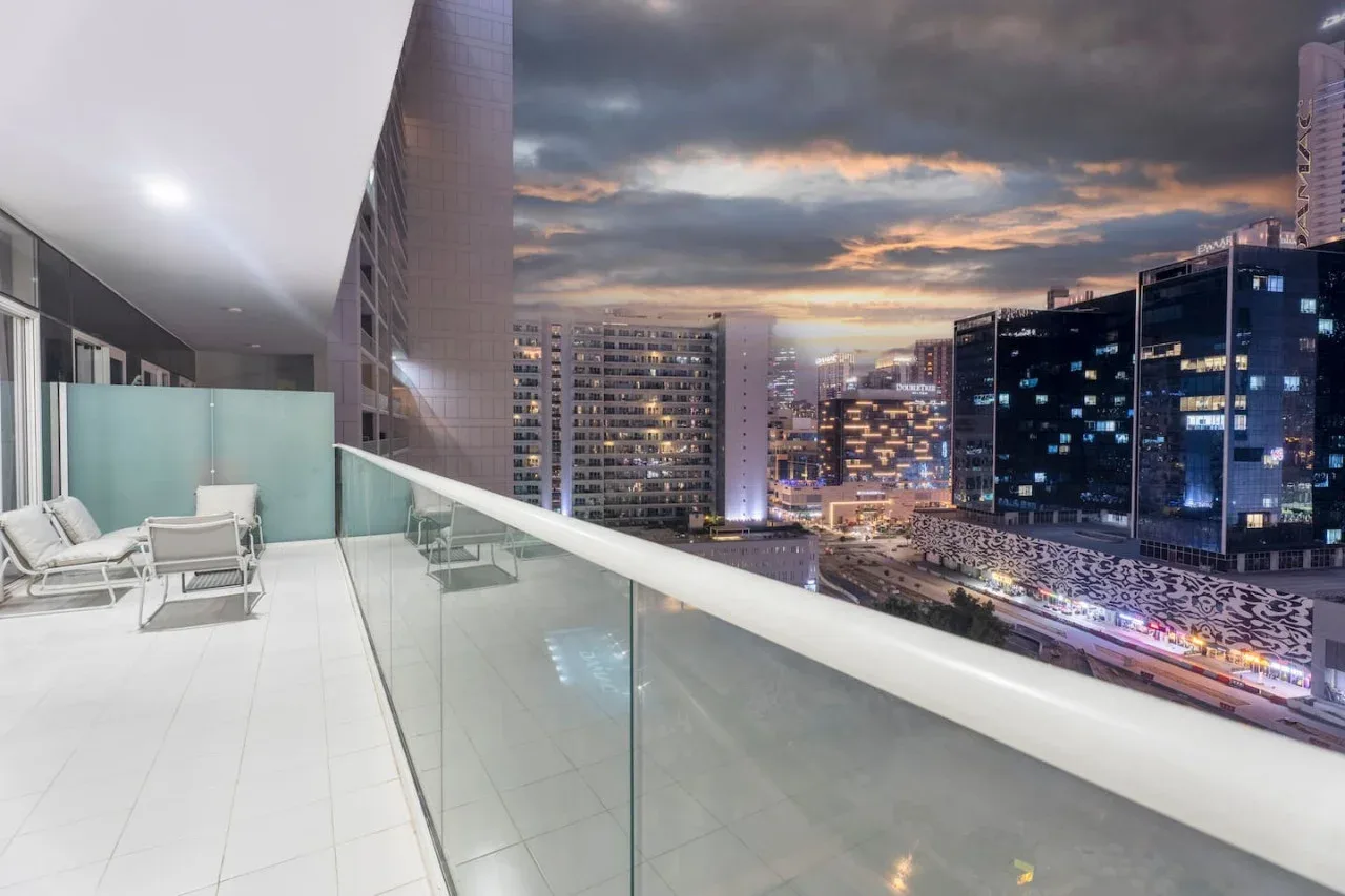 Un balcón con asientos ofrece vistas de edificios iluminados al atardecer.