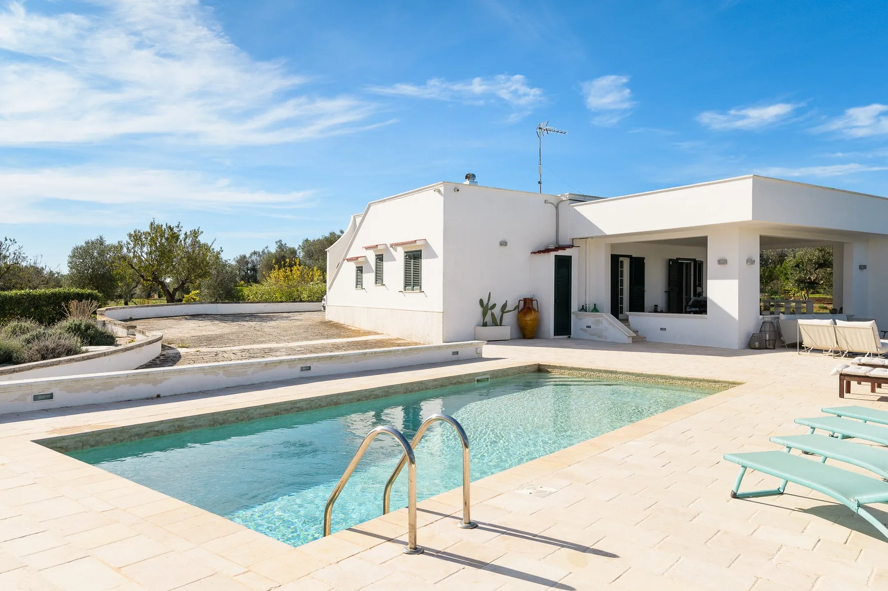 A swimming pool beside a modern white house, with lounge seating on the patio.
