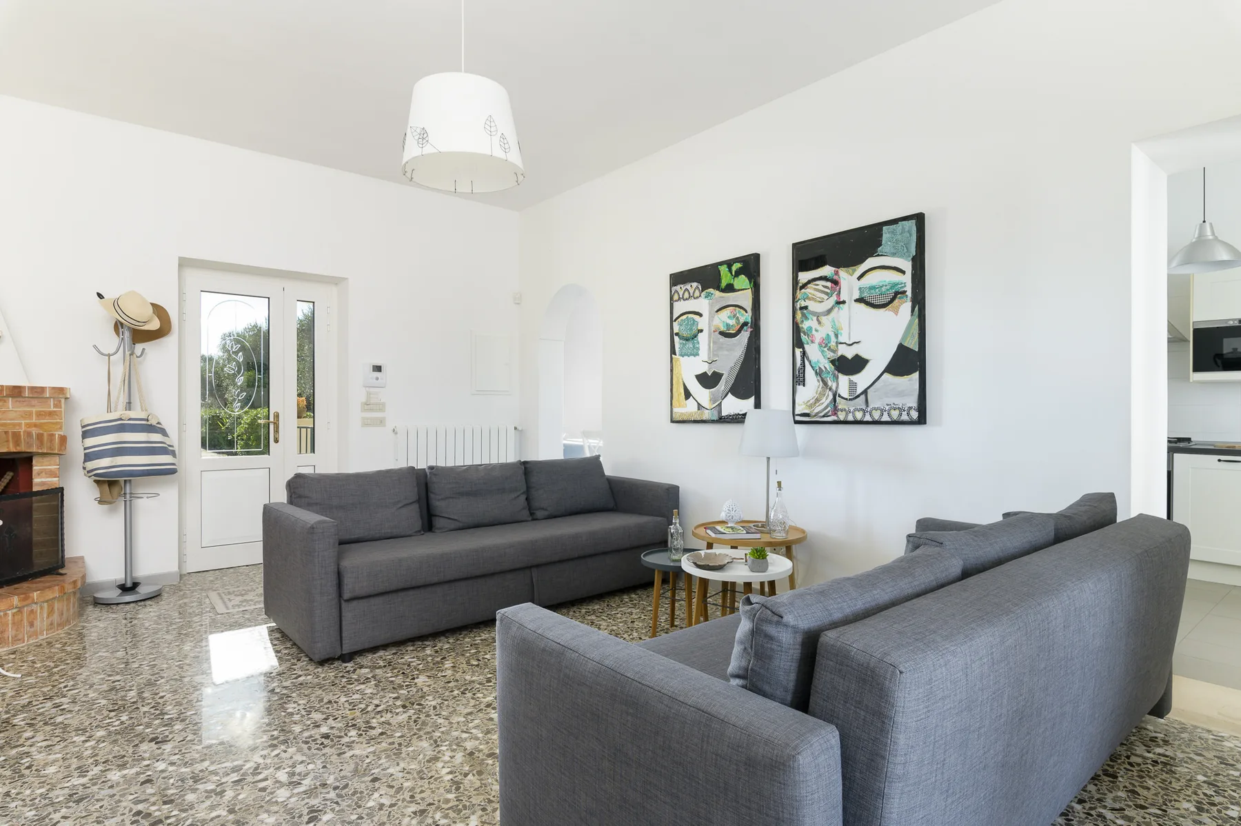 A bright living room with gray seating, colorful wall art, and a small round table.