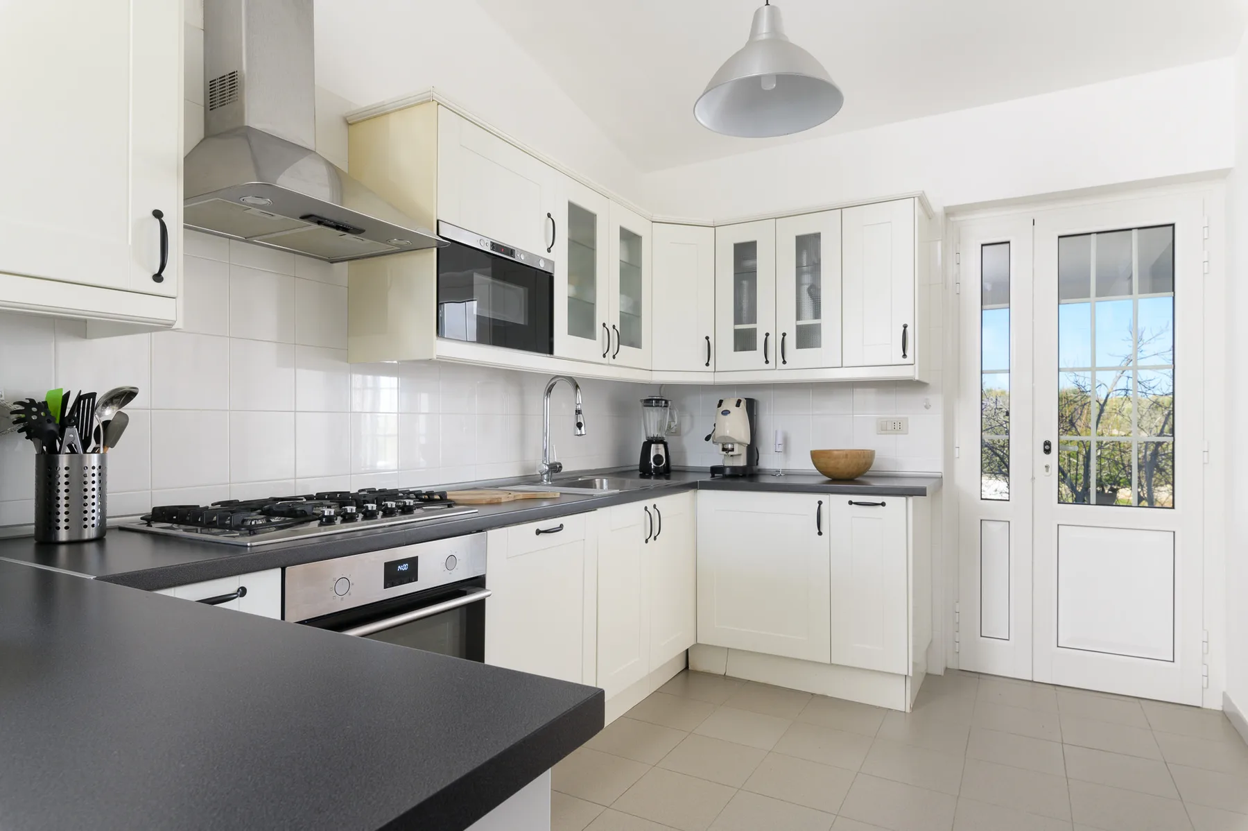 A bright kitchen with white cabinets, dark countertops, and a large window.