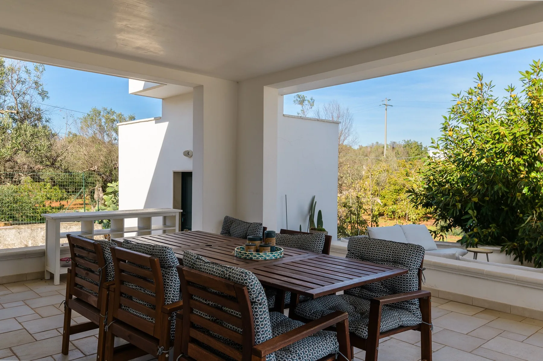 A covered outdoor dining area with a long wooden table and surrounding seating.