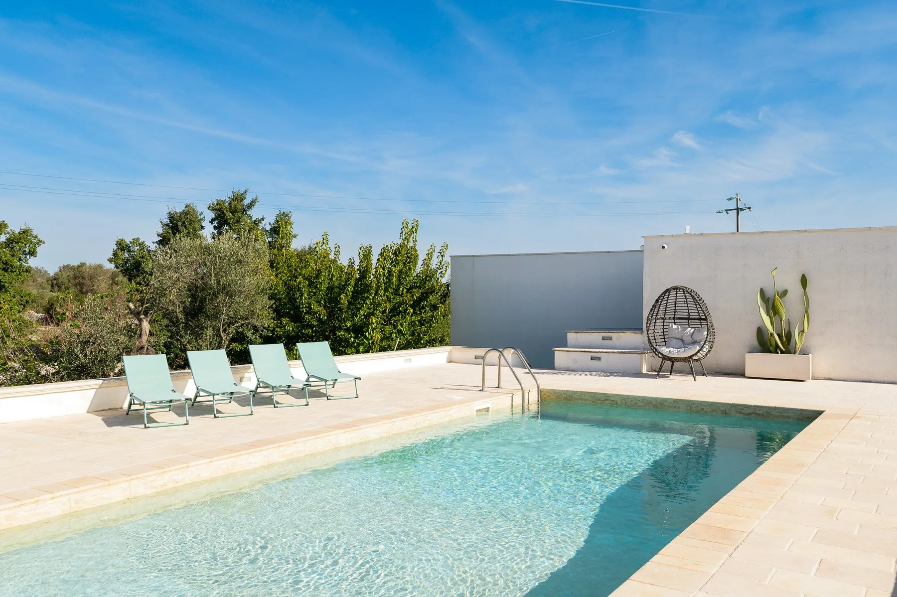 An outdoor swimming pool beside a paved patio with lounge seating.