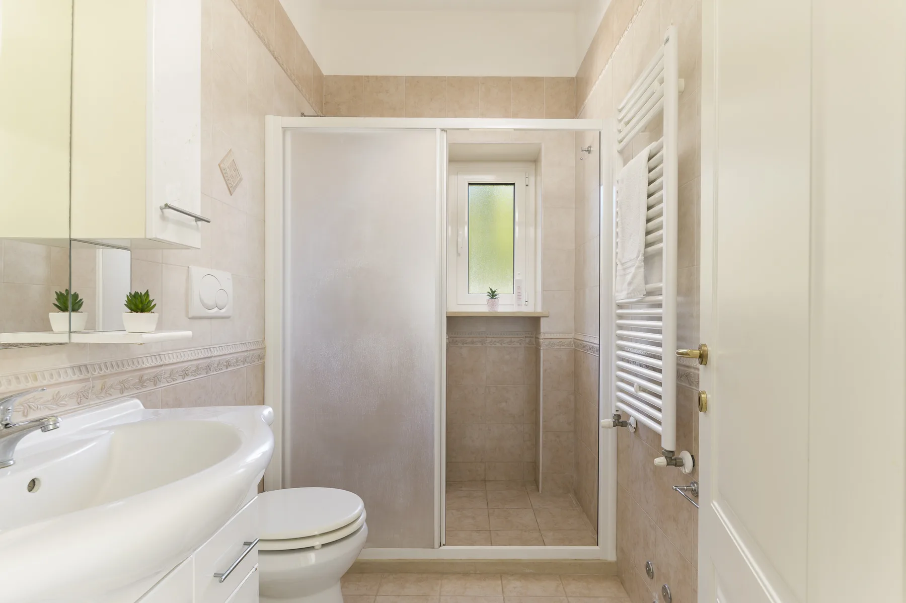 A bright bathroom with a shower, sink, and window.