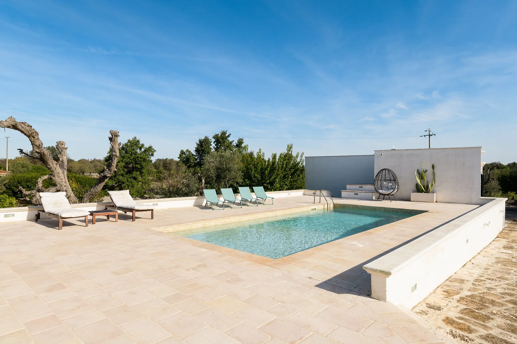 A swimming pool sits in a sunny outdoor terrace with lounge seating.