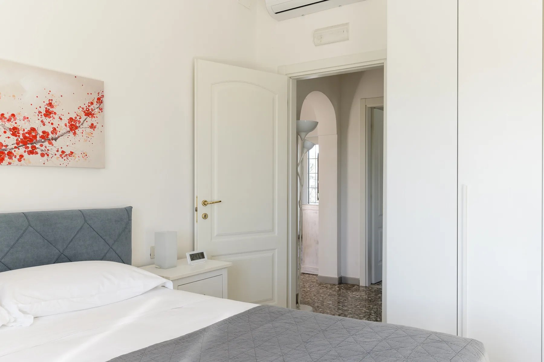 A bright bedroom with a bed, wall art, and an open doorway.