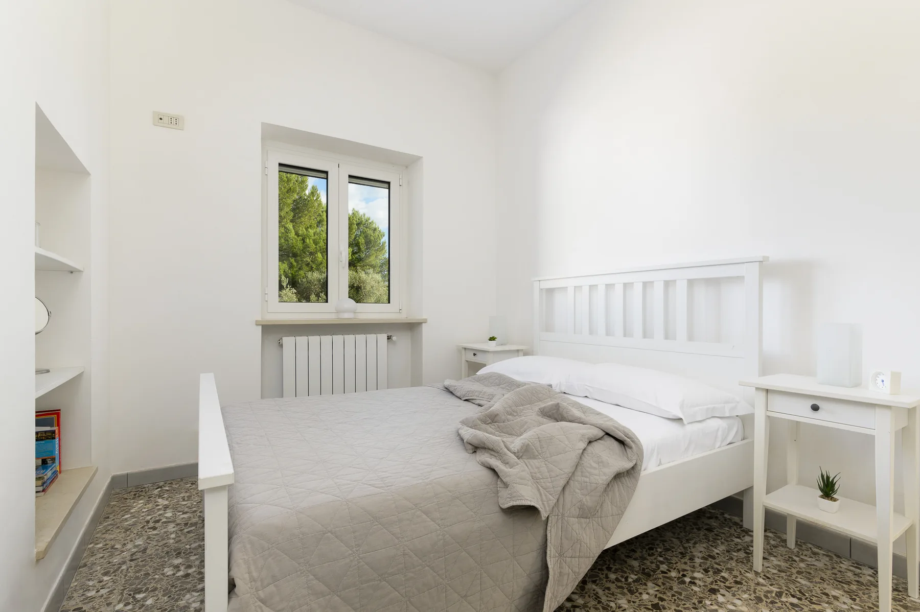 A bright bedroom with a white bed beside a window.