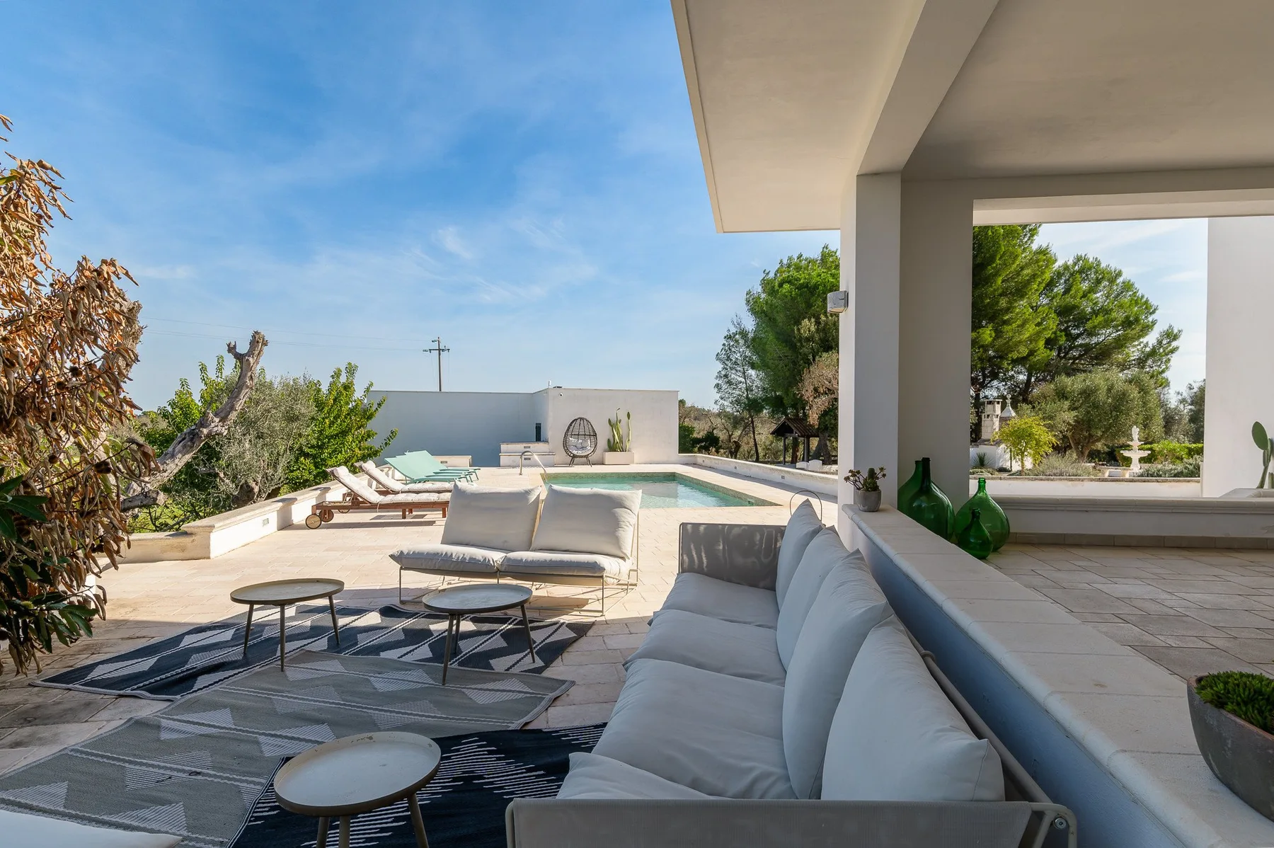 An outdoor lounge beside a swimming pool, with cushioned seating and trees.