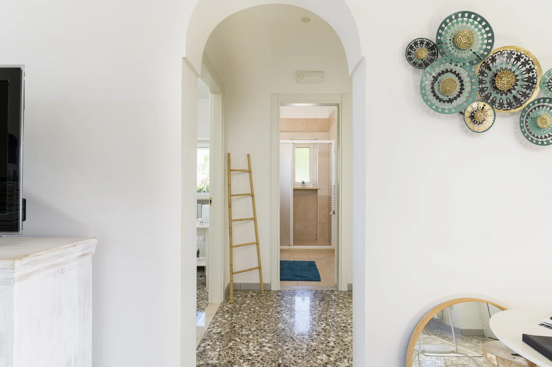 A bright hallway with an arched opening, patterned floor, and wall decorations.