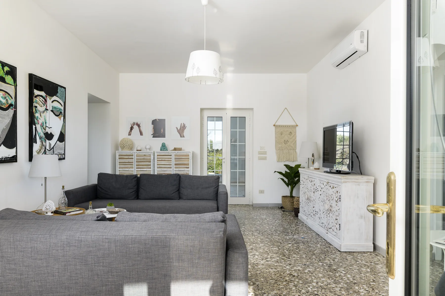 A bright living room with gray seating, a television, and a glass door.