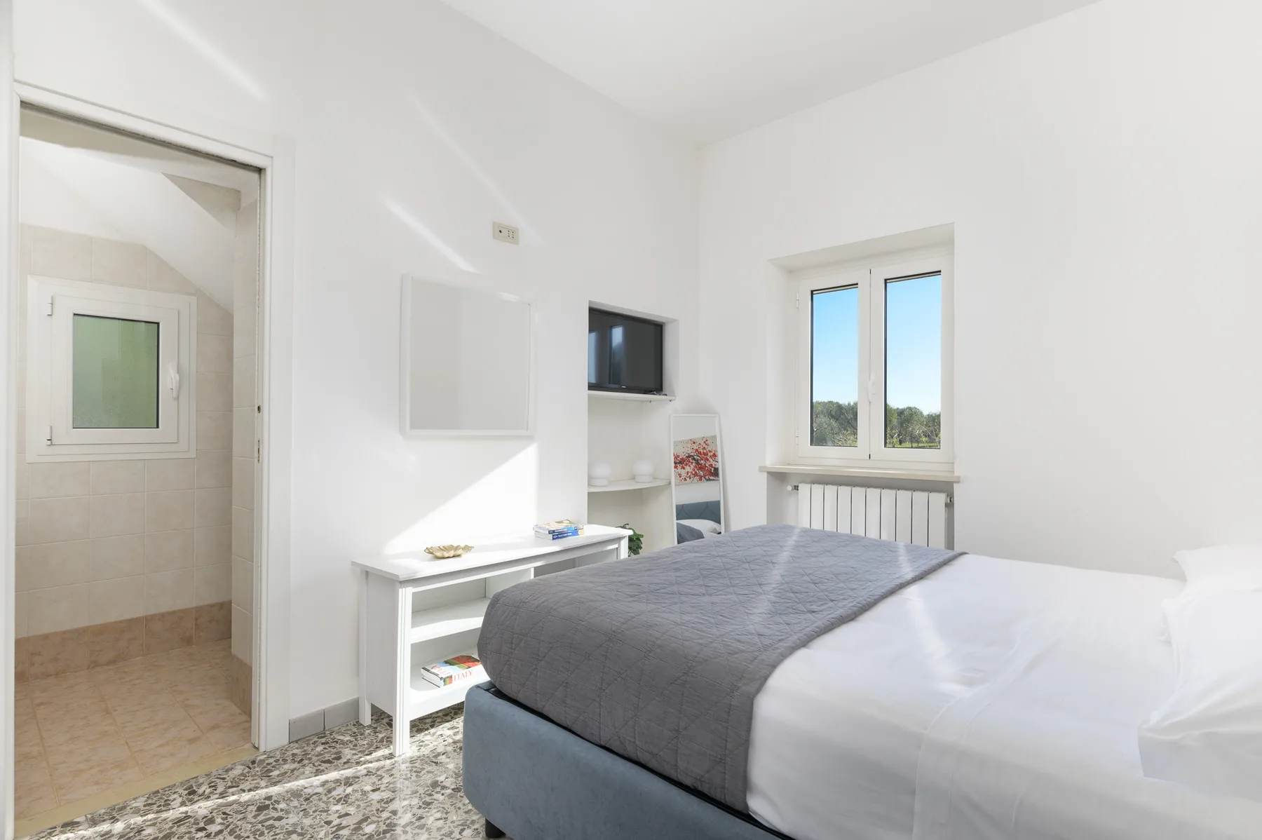 A bright bedroom with a bed, a small desk, and a window.