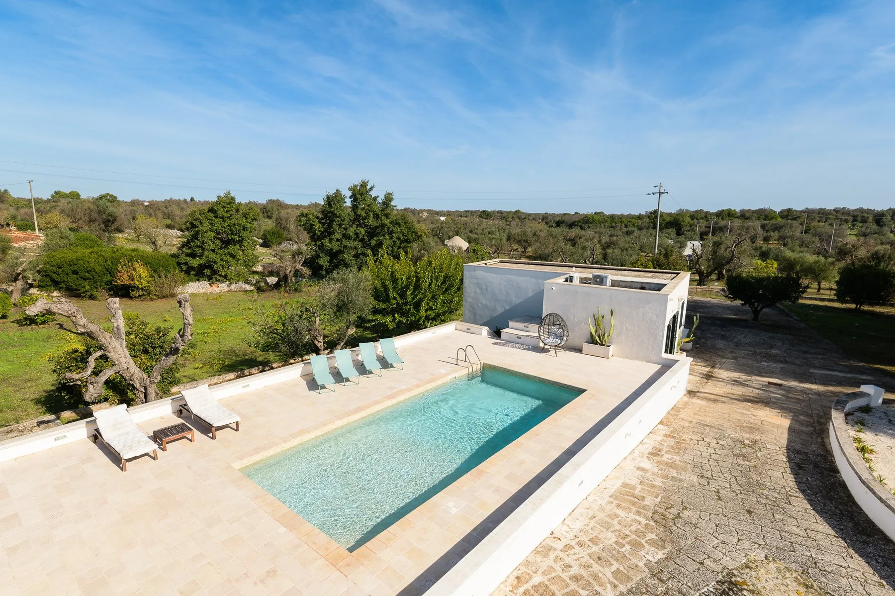 An outdoor swimming pool sits beside a small poolside structure and lounge seating.