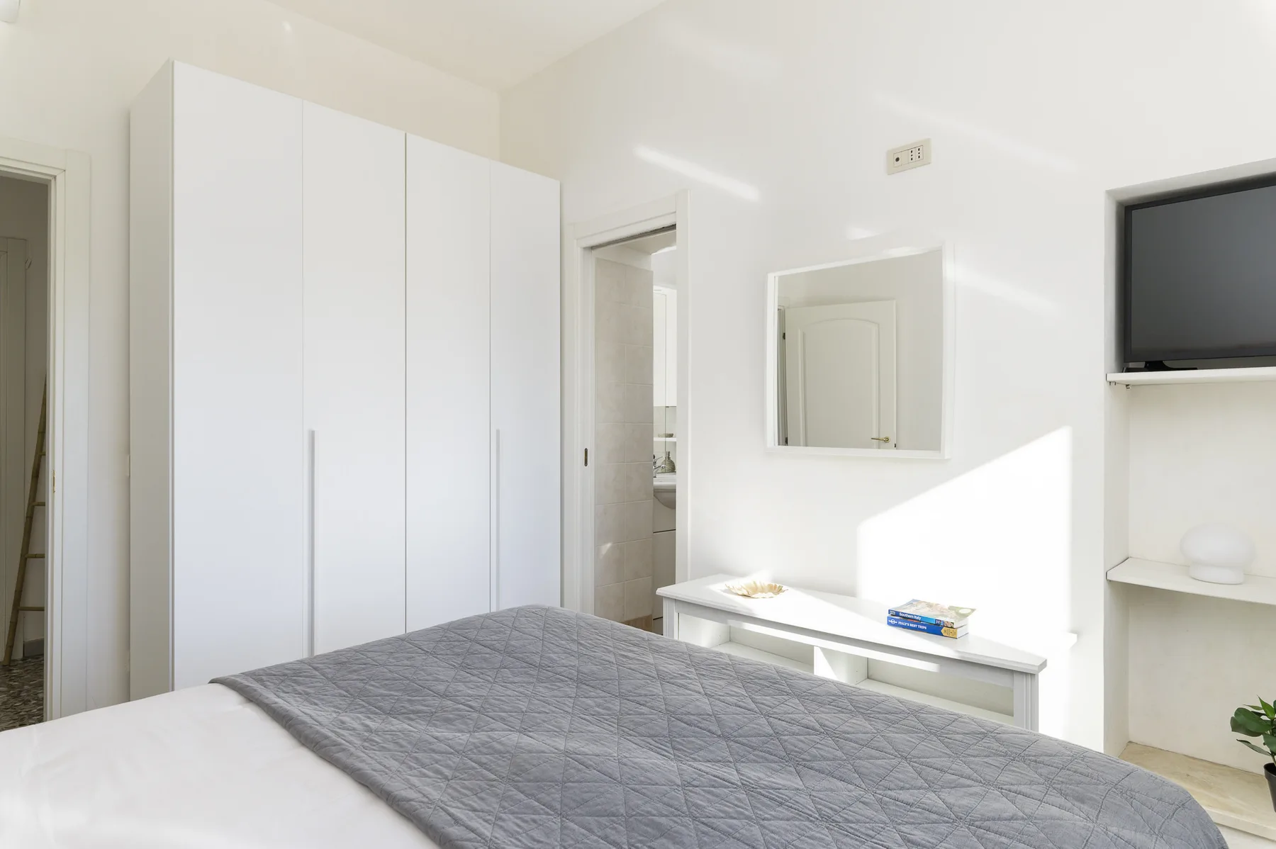 A bright bedroom with a bed, white wardrobe, and wall-mounted television.