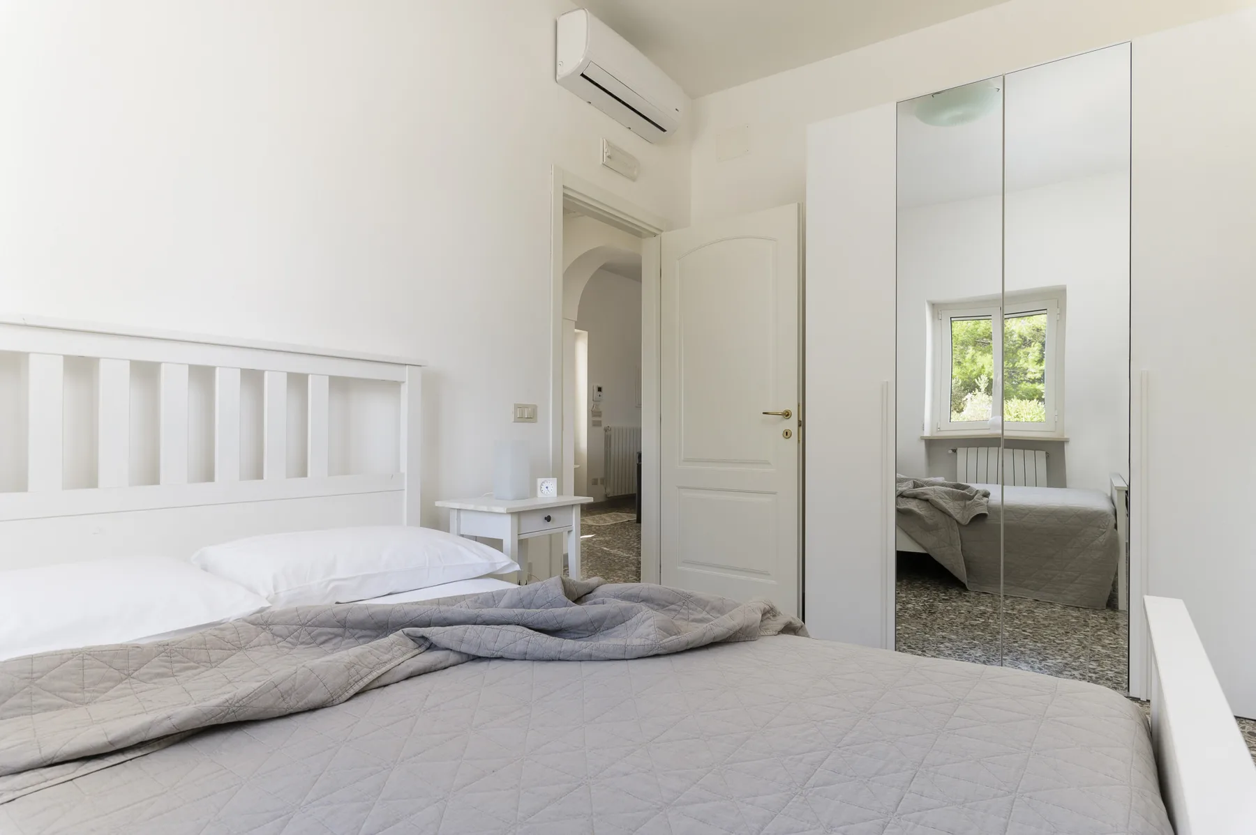 A bright bedroom with a bed and mirrored wardrobe.