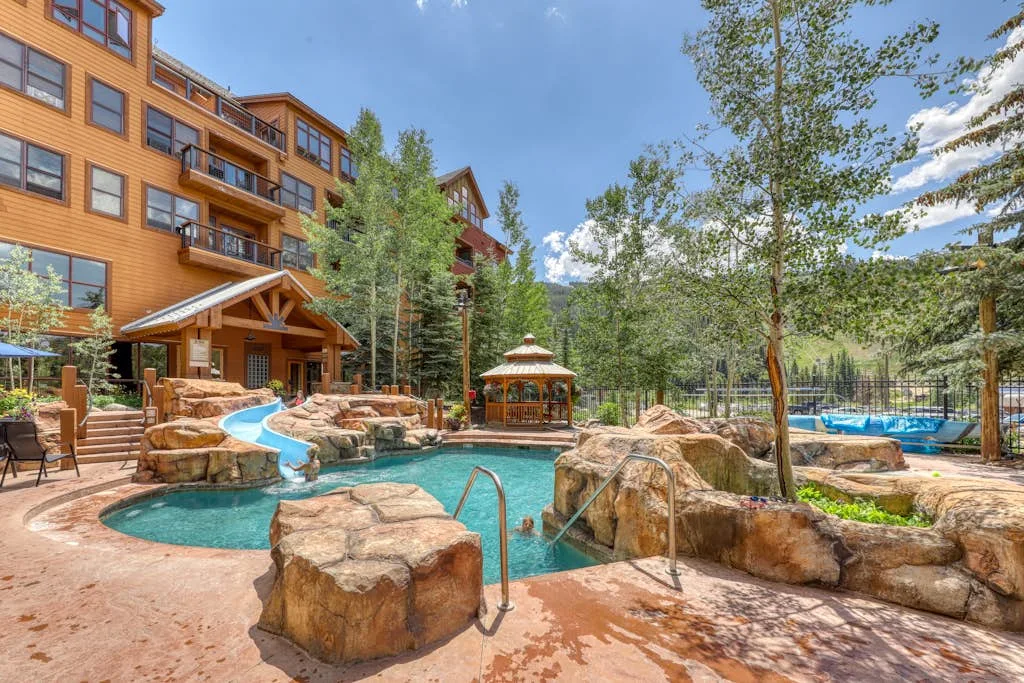 An outdoor pool winds through a landscaped courtyard beside a multi-story building.