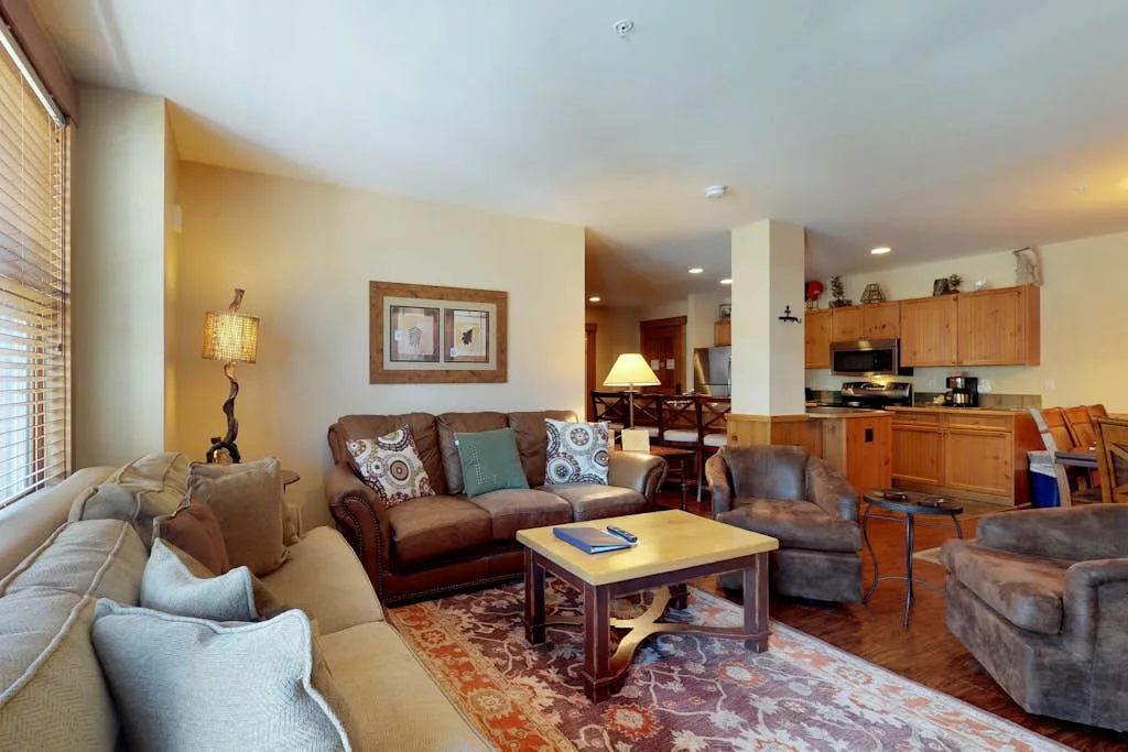 A living room with seating around a coffee table, open to a kitchen.