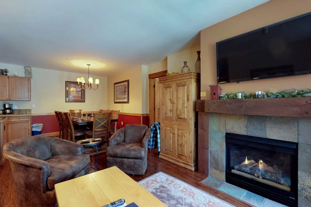 A living room with seating, a dining table, and a fireplace beneath a television.